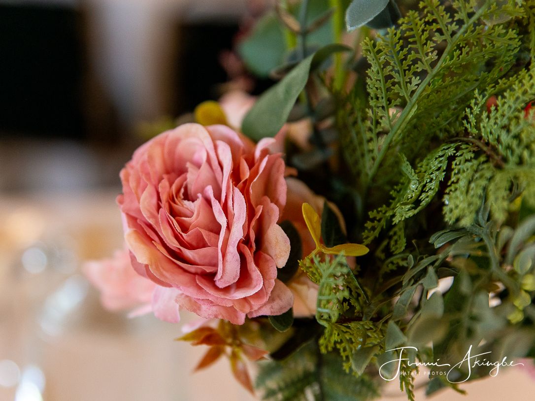 A soft pink rose bloom with delicate petals nestled among green foliage in an elegant floral arrangement.