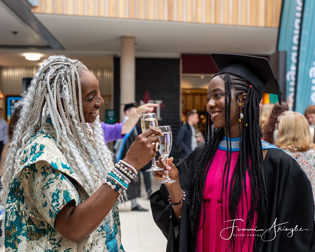 Two beautifully dressed ladies share a celebratory toast at a graduation ceremony with smiles and joy.