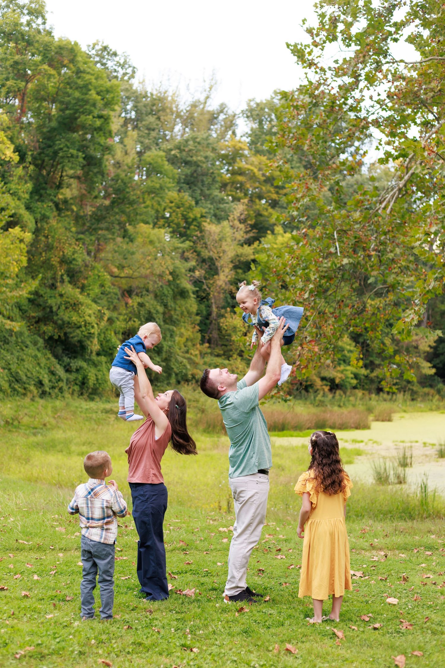 parents tossing children into the air during playful family session in lush green setting