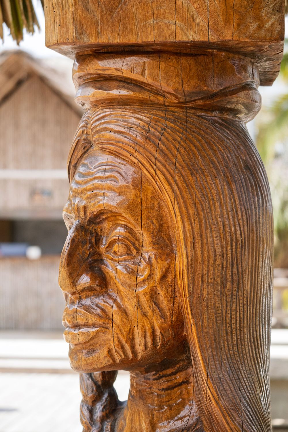 Carved wooden native face sculpture on decorative pillar with detailed features.