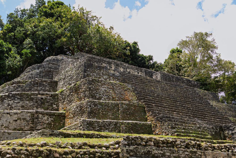 Wide view of stepped Maya pyramid ruins surrounded by green jungle landscape.