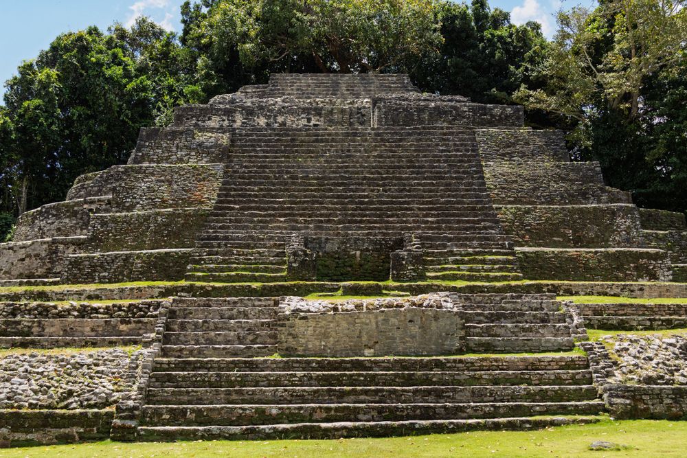 Panoramic view of ancient Maya temple ruins with stepped architecture against blue sky.