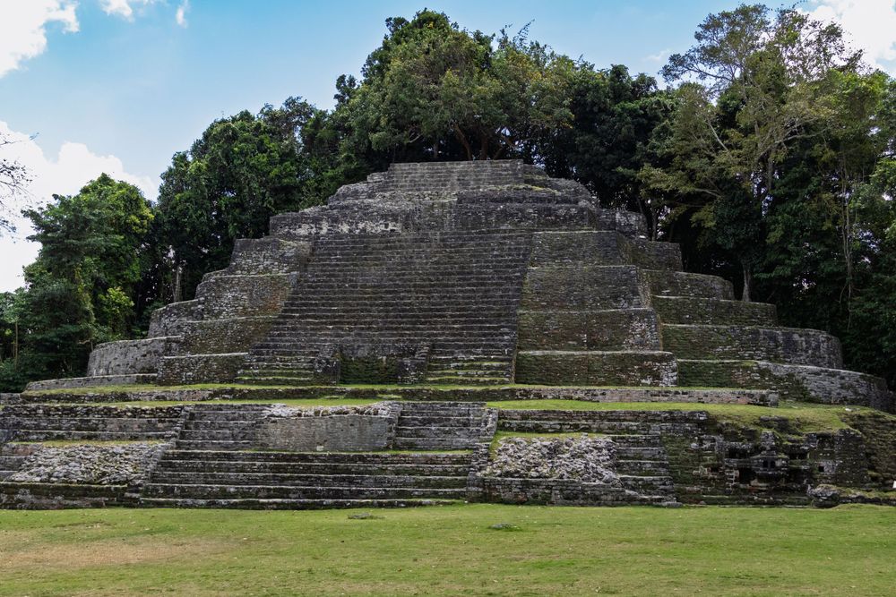 Ancient Mesoamerican stepped pyramid ruins with green grass field in the foreground.
