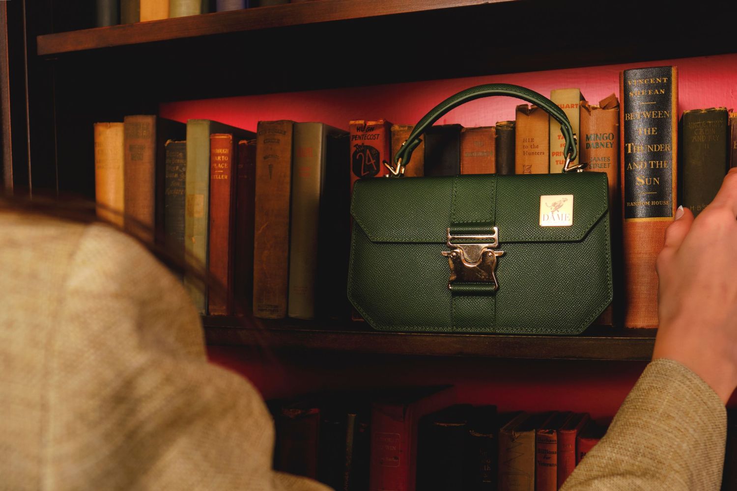 Green leather handbag displayed on wooden bookshelf with warm lighting.