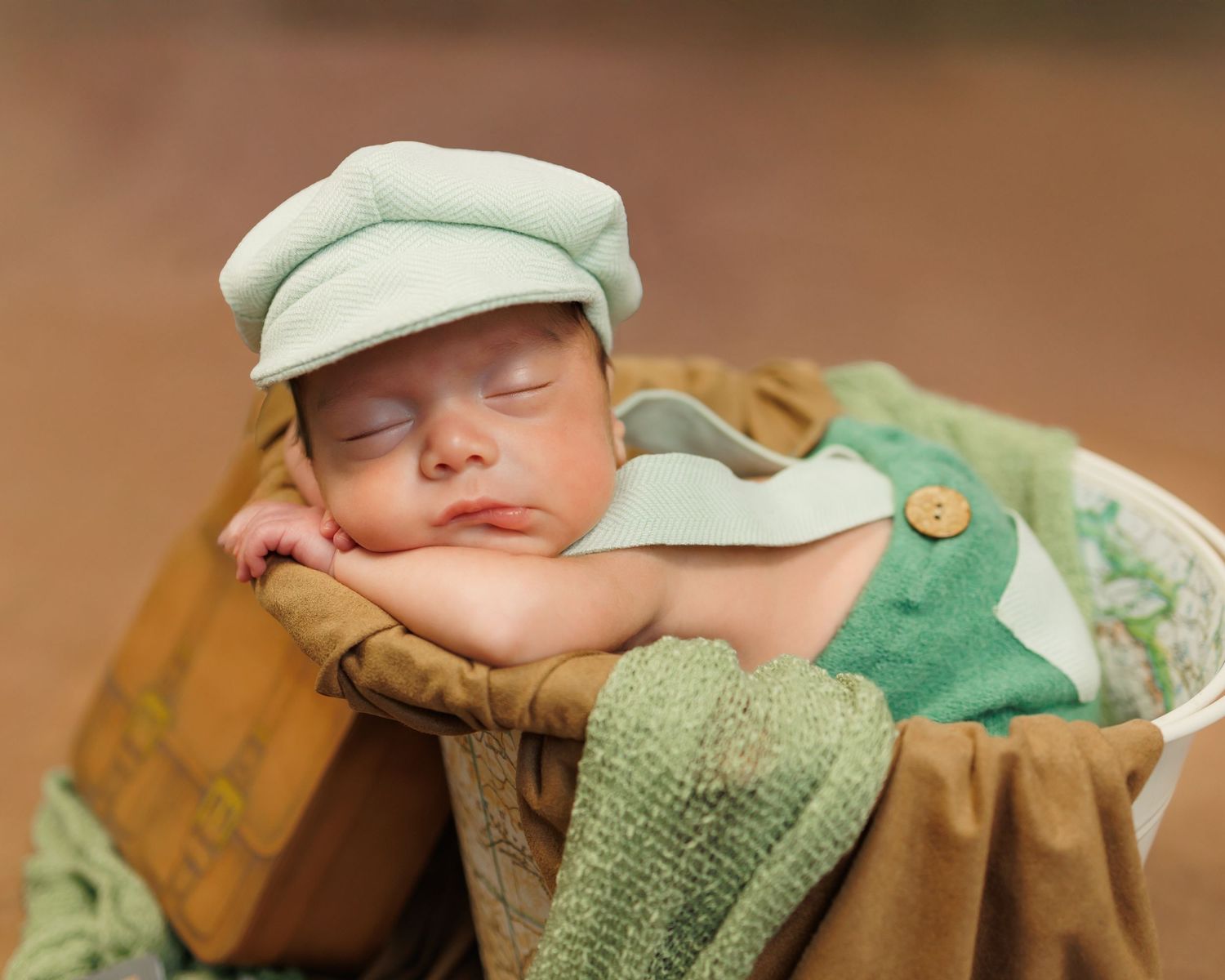 A sleeping baby wearing a green knit sweater and floral headband rests peacefully in soft lighting.