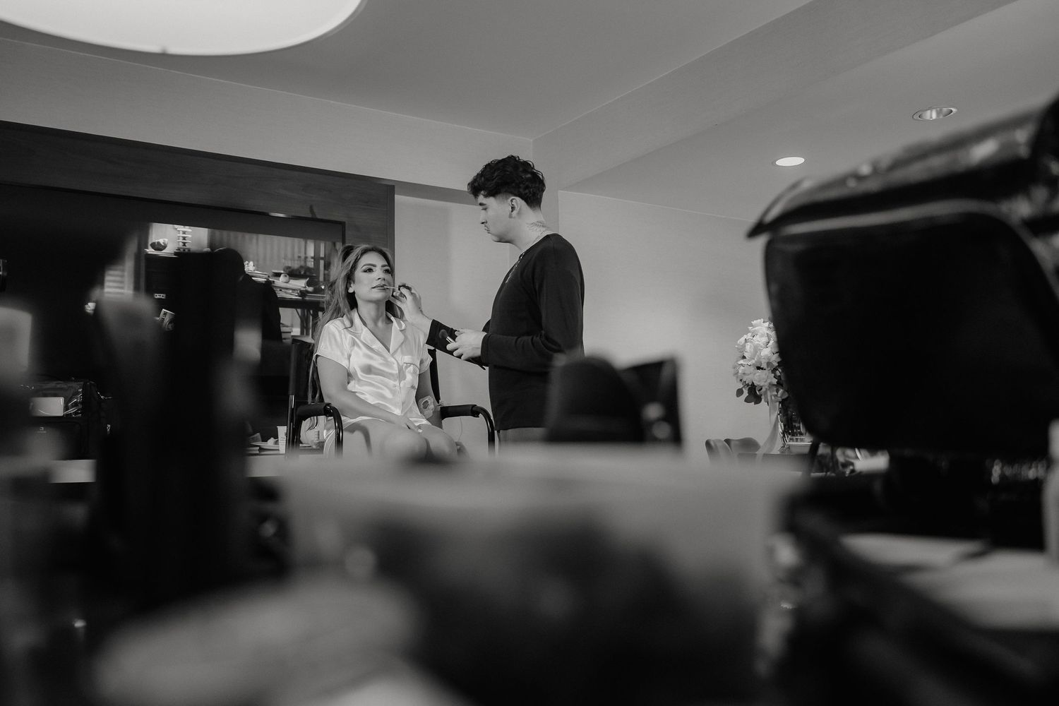 A black and white candid photograph captures a moment between two people in a dimly lit indoor setting.