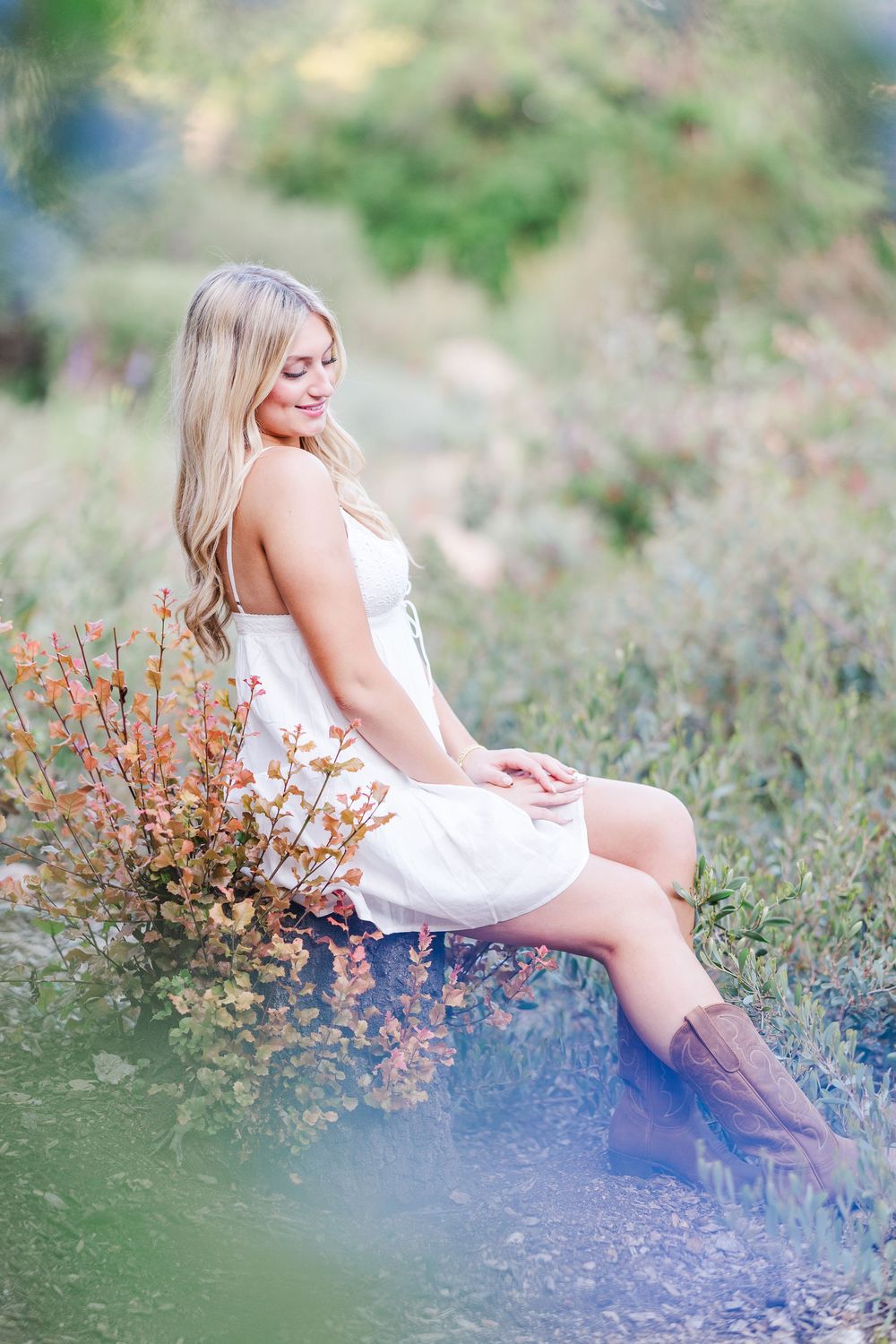 A figure in a white dress sits gracefully among wildflowers and tall grasses on a dreamy summer afternoon.