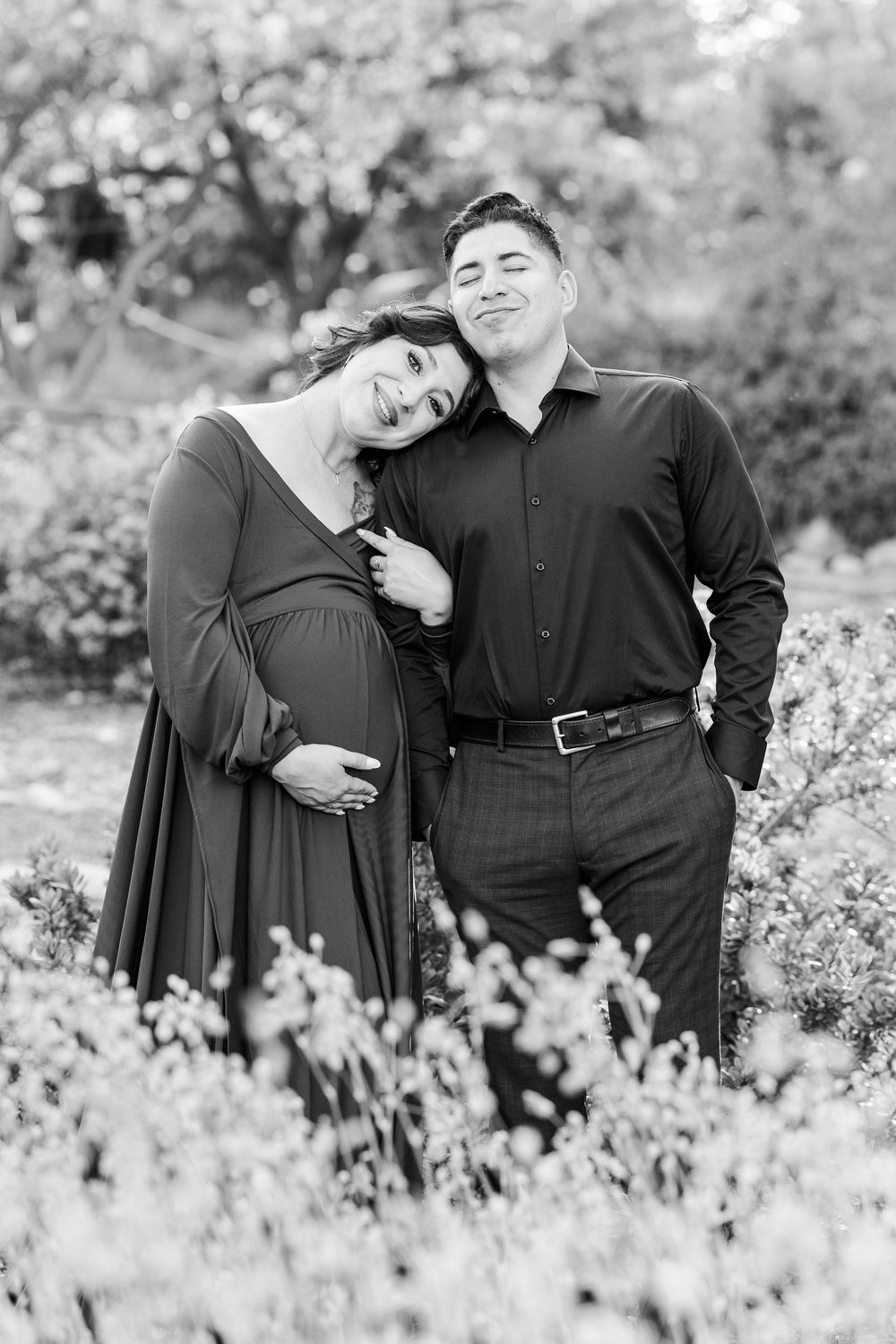 Black and white maternity photo of a couple embracing outdoors with blooming cherry trees in the background.