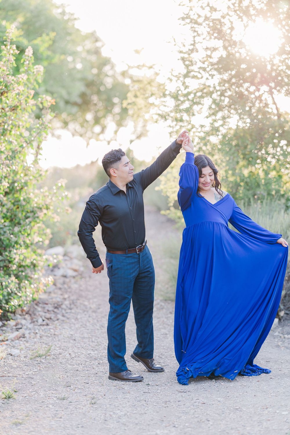 A couple dancing together outdoors on a dirt path, with the woman wearing a flowing royal blue dress in sunlit scenery.
