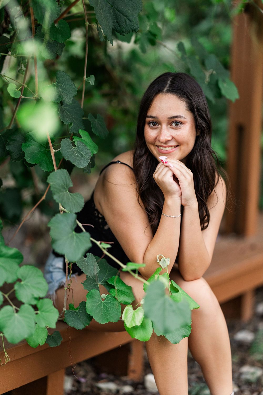 Portrait with green grapevine leaves framing a subject posing on a wooden deck in natural outdoor lighting.