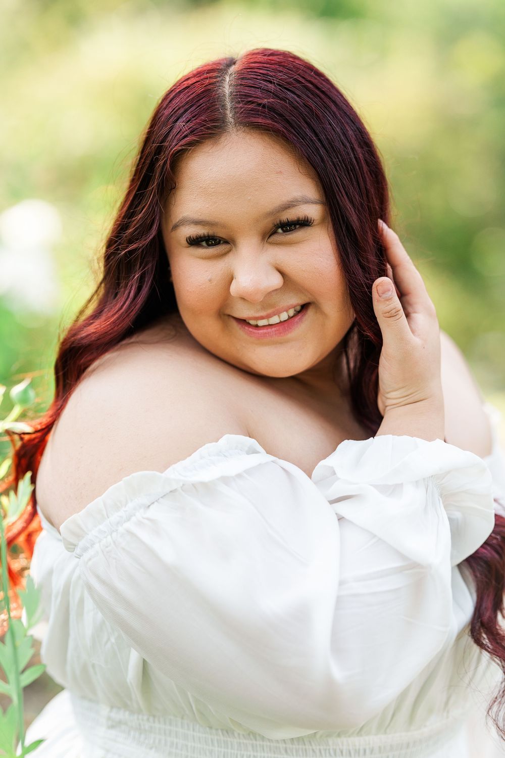 Portrait series of woman with burgundy hair wearing white blouse smiling in outdoor garden setting.