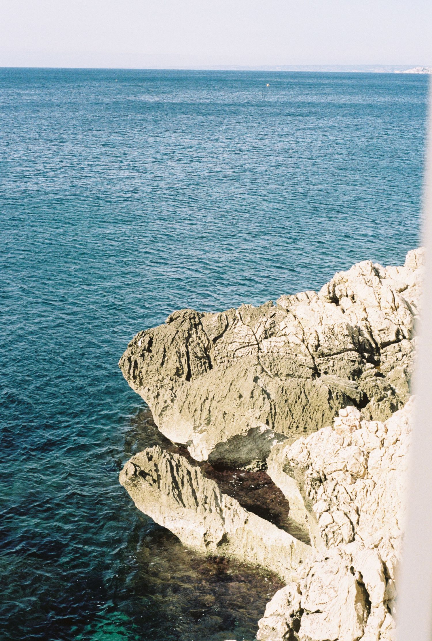 Rugged limestone cliffs meet turquoise Mediterranean waters on a sunny coastline.