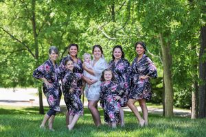Bridesmaids in matching floral robes pose playfully on grass with the bride.