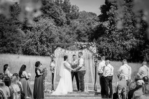 Outdoor wedding ceremony under a wooden arch with guests seated on both sides.