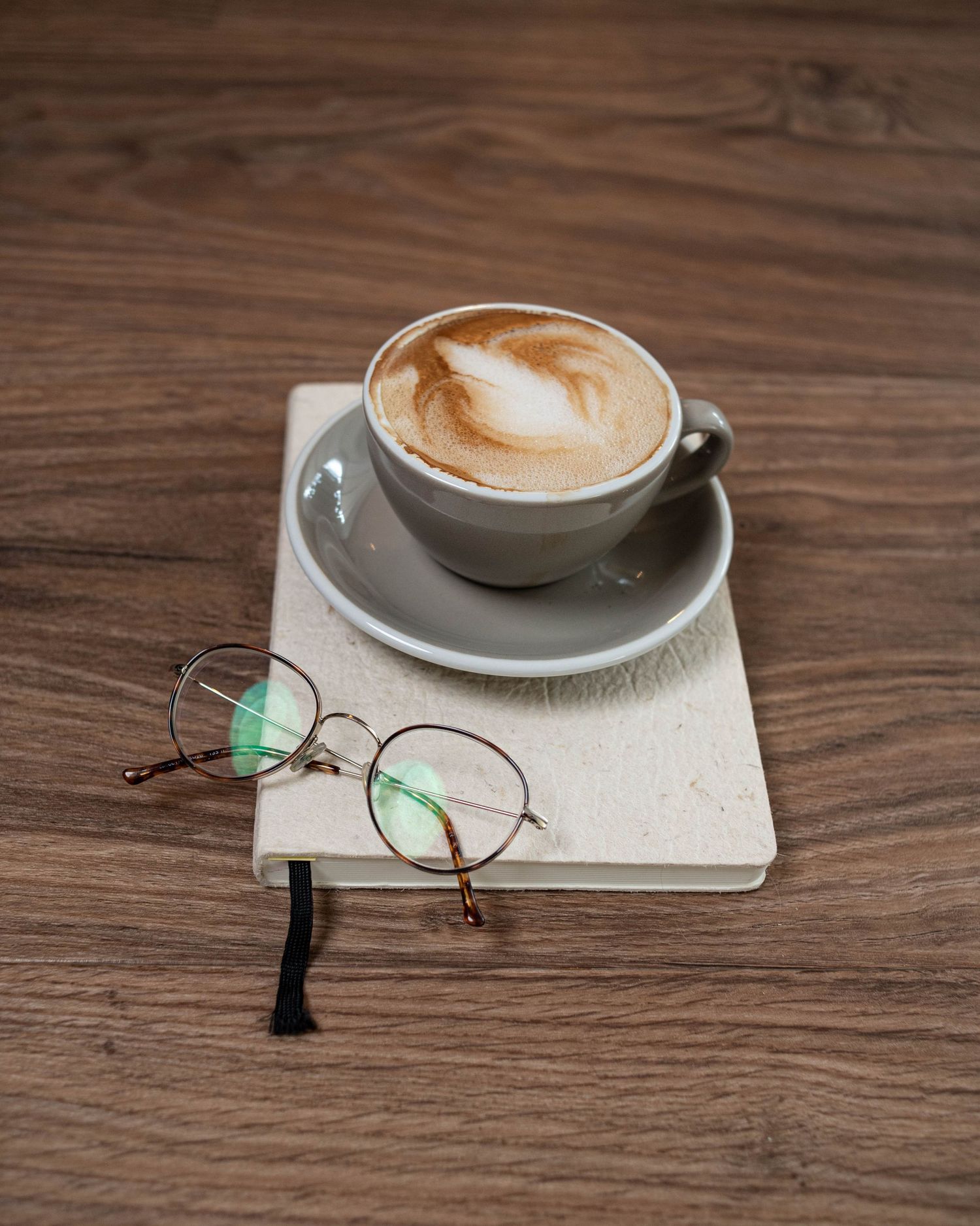 A coffee cup with foam art sits next to round glasses on a light colored surface.