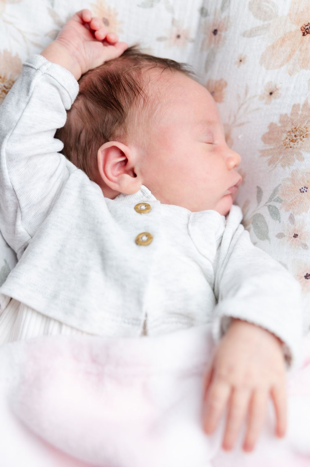 Sleeping newborn baby wearing white clothing lies on floral patterned bedding.