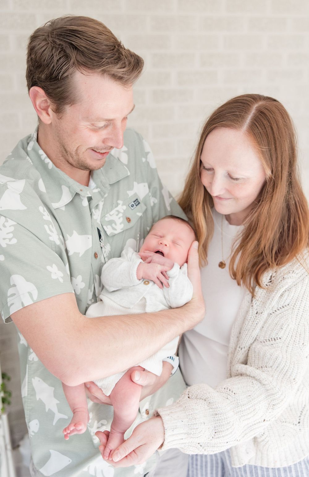 Family in soft neutral colors admiring their newborn baby in a bright airy room.