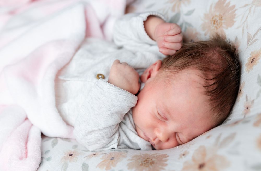 Peaceful newborn baby sleeping soundly on soft pink and white bedding.