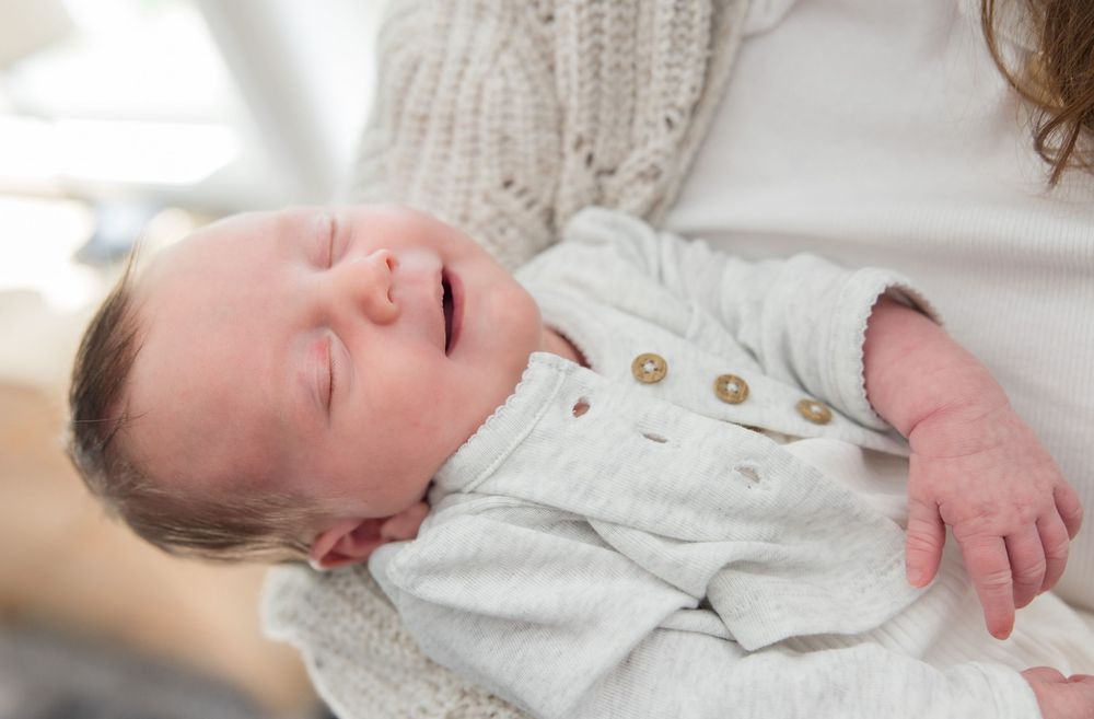Sleeping newborn baby wearing white buttoned outfit resting on soft knitted blanket.