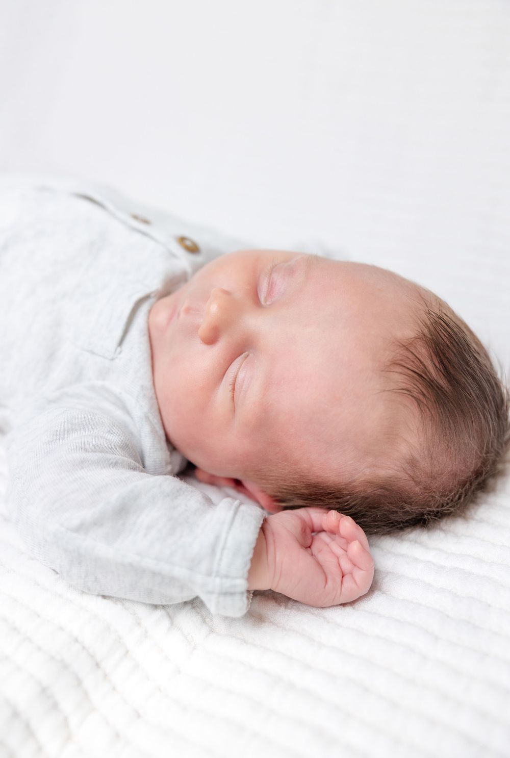 Peaceful sleeping newborn baby in white onesie resting on soft white bedding.