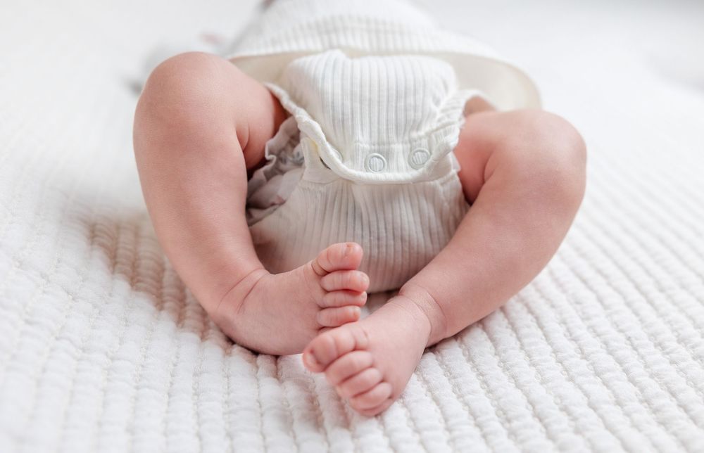 Close up view of tiny baby feet in white knitted clothing on textured fabric.