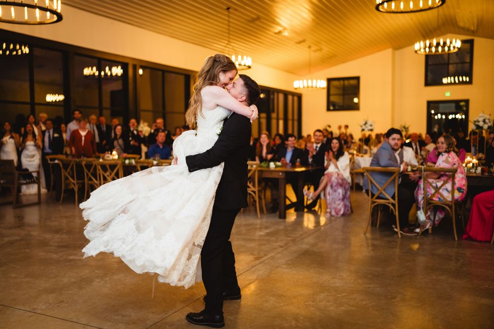 Bride and groom share a romantic dip while dancing at their wedding reception in a warmly lit ballroom.