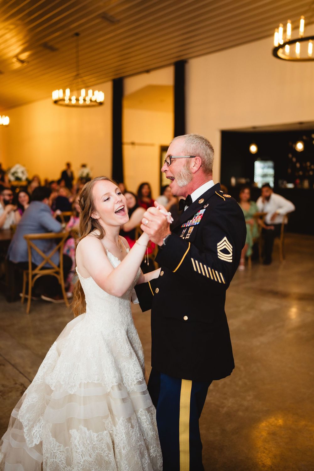 A joyful moment on the dance floor shows a bride in a white gown dancing with a uniformed serviceman at a wedding reception.