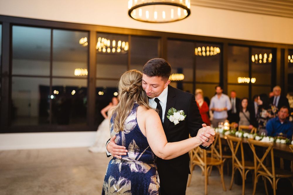 A couple shares a romantic dance together at an elegant indoor venue with mood lighting and wooden chairs in the background.