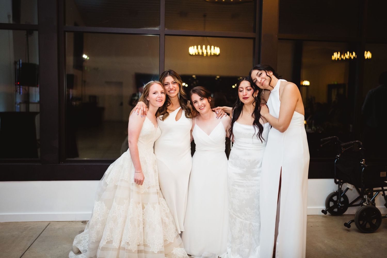 A row of women in white dresses stand together laughing and smiling during a formal event.