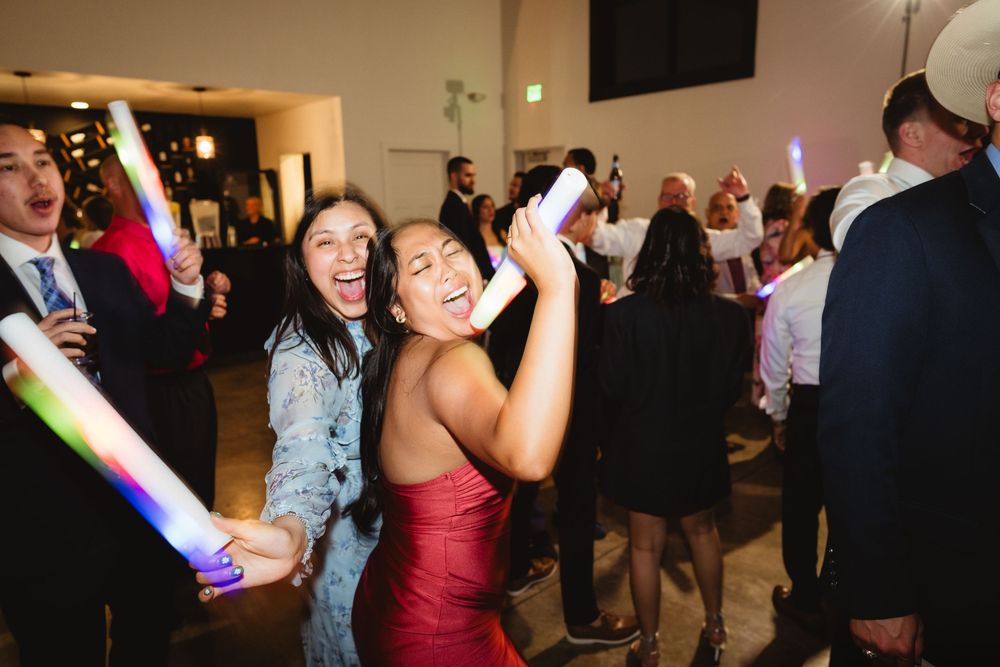 Party guests celebrate on dance floor with LED foam glow sticks at evening reception.
