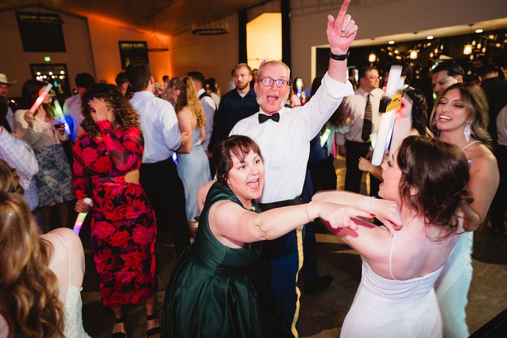 Wedding guests dance joyfully together on a dimly lit dance floor during an energetic reception celebration.