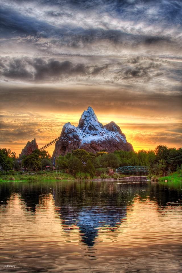 Expedition Everest mountain peak at Disney's Animal Kingdom reflects in calm waters during a dramatic sunset.