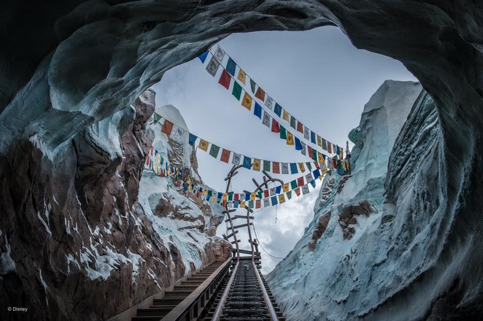 Prayer flags stretch across a stairway leading out of an icy blue glacial cave in the mountains.
