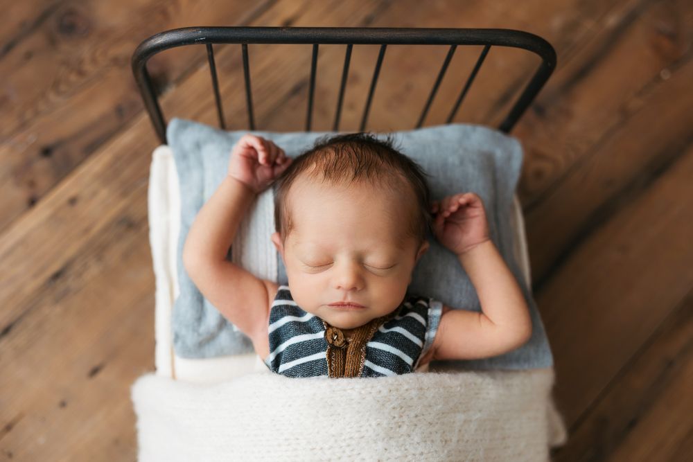 Sleeping baby in striped outfit lying on blue pillow in vintage metal bed frame.
