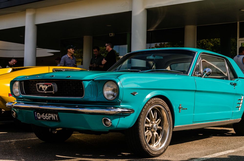 Restored turquoise 1965 Ford Mustang with custom wheels displayed at a car show.