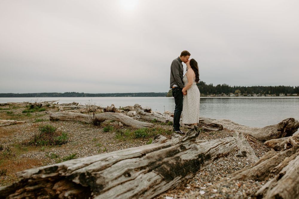 A romantic moment shared on fallen logs at the edge of a moody waterfront landscape.