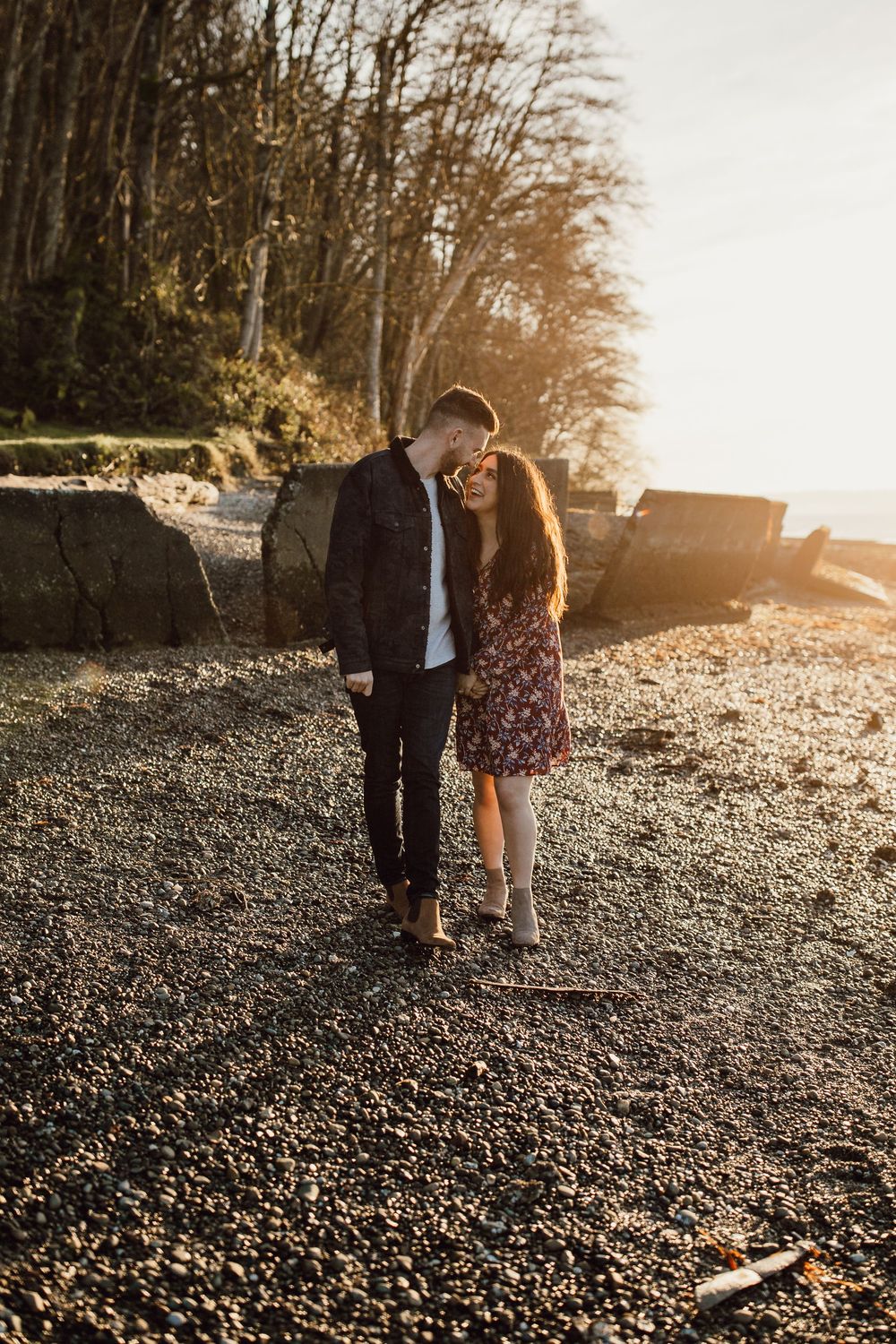 A couple enjoying a romantic sunset moment on a rocky beach path during golden hour.