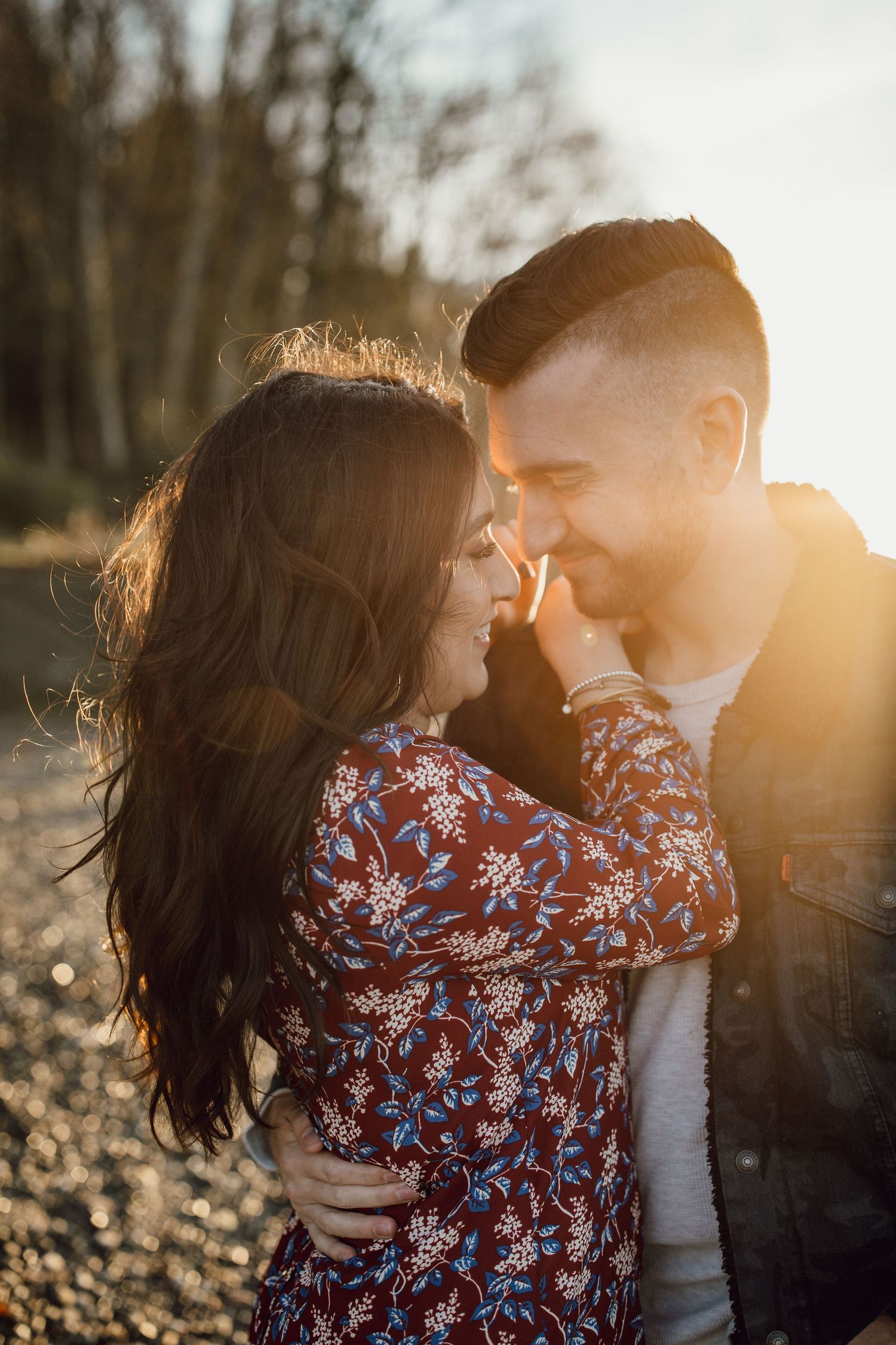A romantic sunset photoshoot features a couple embracing in warm golden light with a floral dress and natural backdrop.