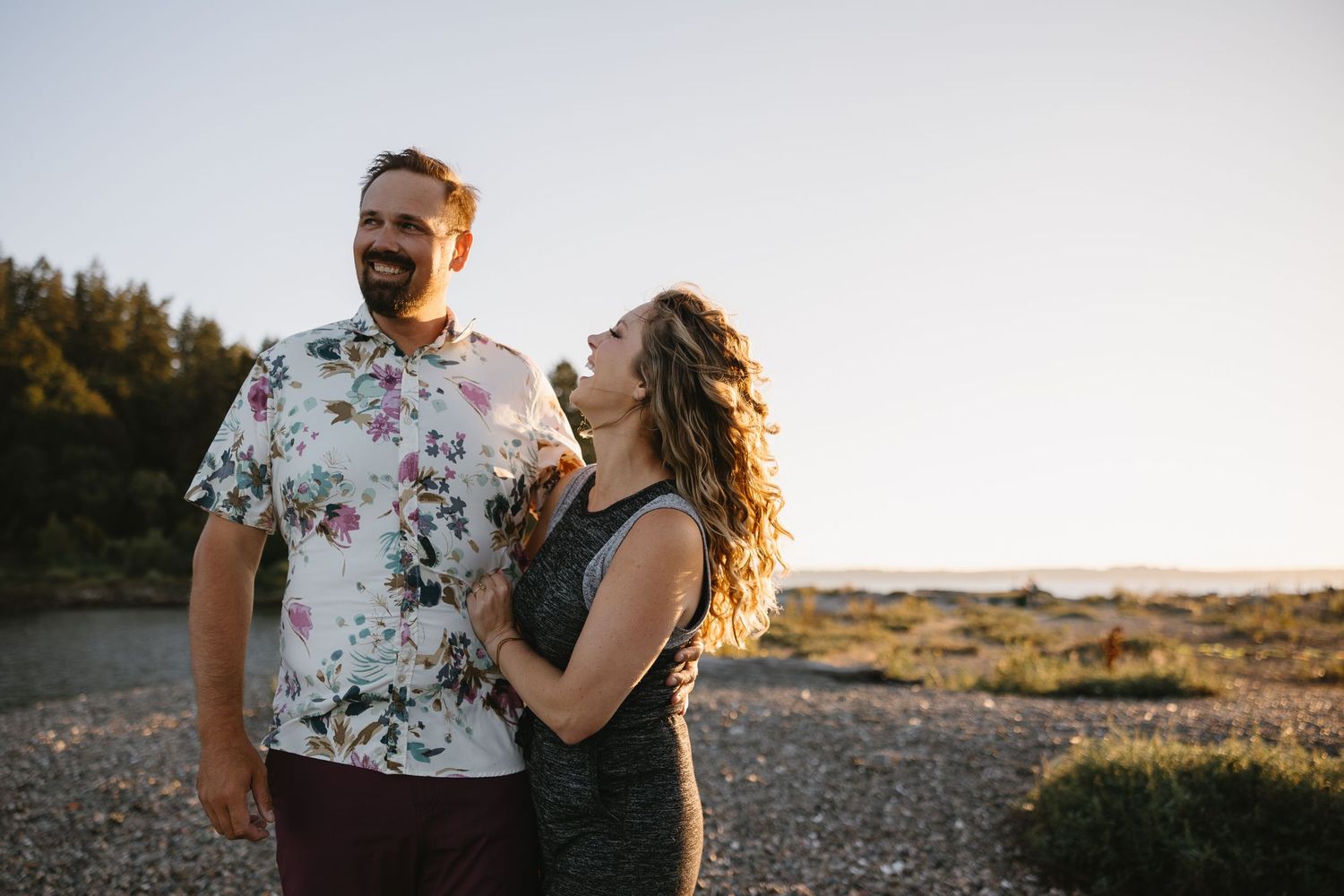 A couple shares a joyful moment together at sunset, with the person in a floral shirt and one in a black top.
