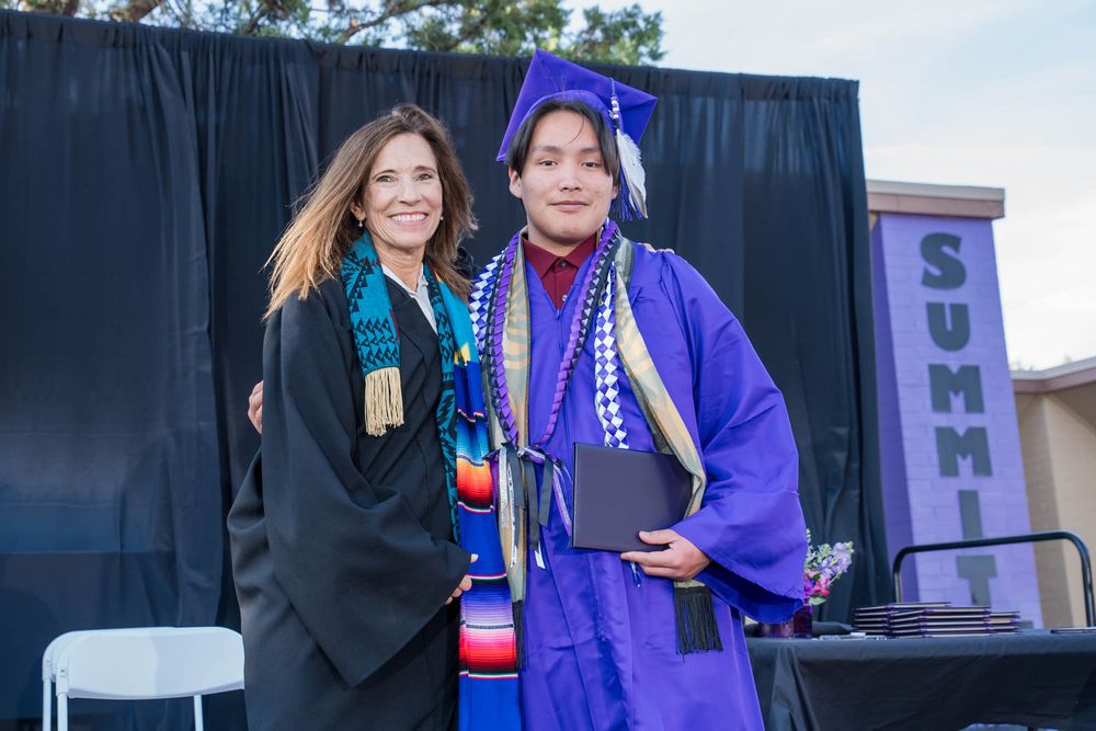 Graduate in purple academic regalia and black graduation gown stand together at commencement ceremony.