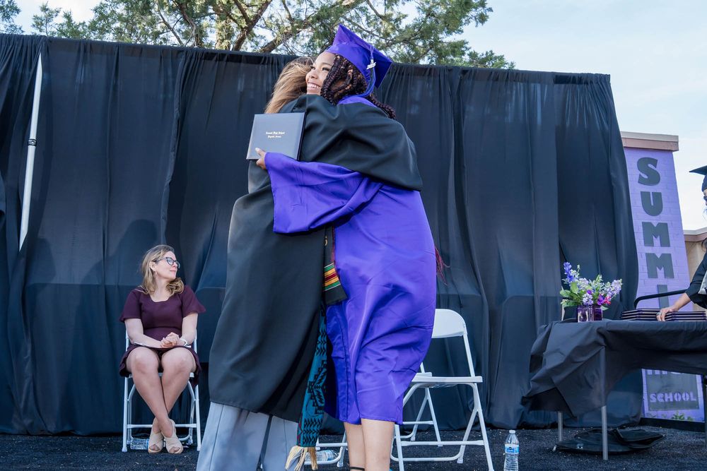A graduate in purple and black academic regalia stands on stage during a commencement ceremony.