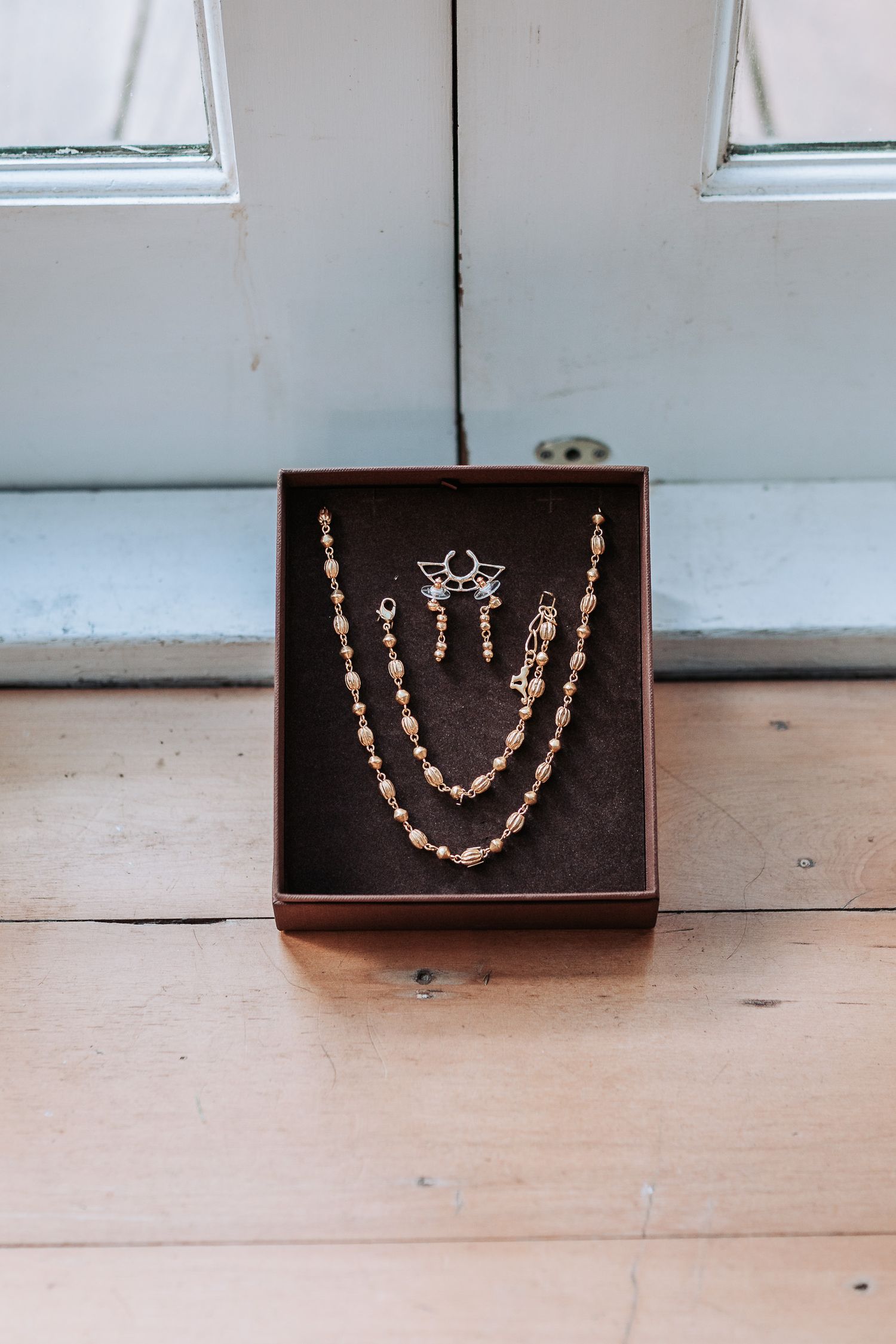 Vintage-style pearl necklace and earring set displayed in a dark brown jewelry box on a wooden floor.