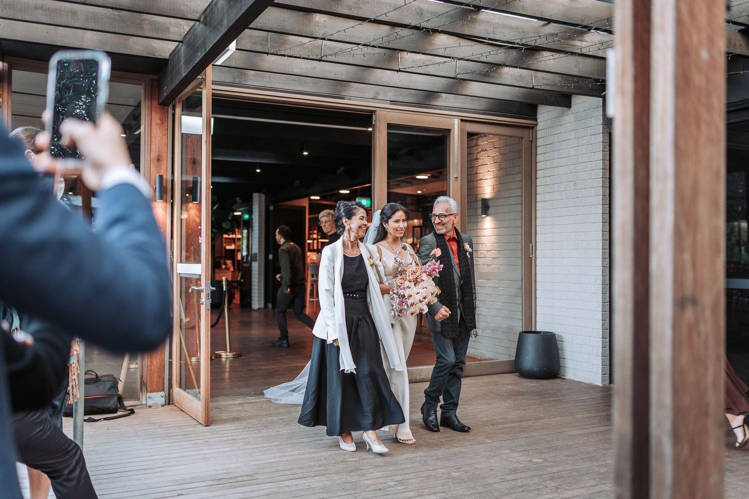 A group poses together outside a building entrance while someone takes their photo with a phone.