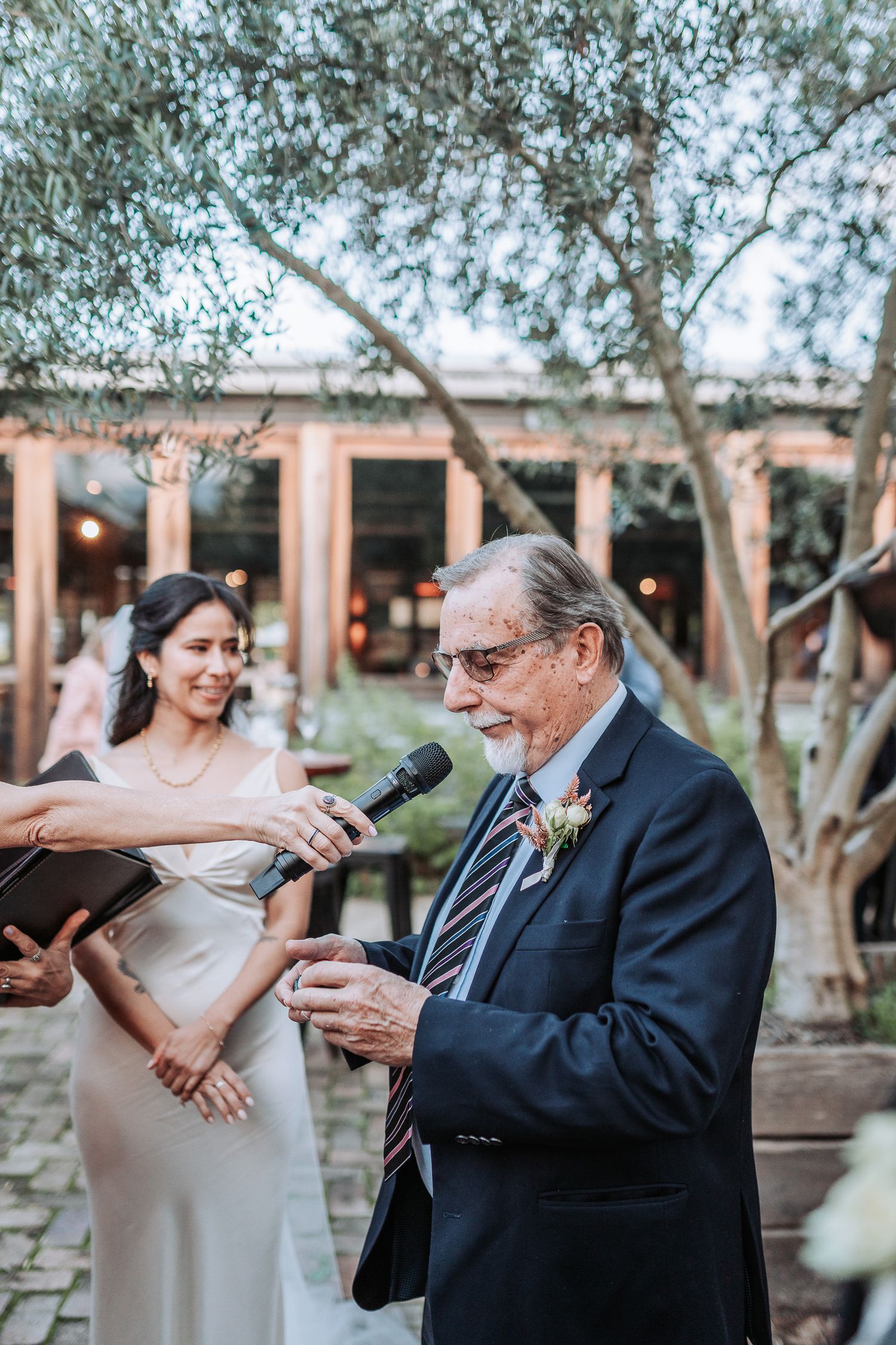 A tender outdoor wedding moment captured at a venue with olive trees and warm evening lighting.