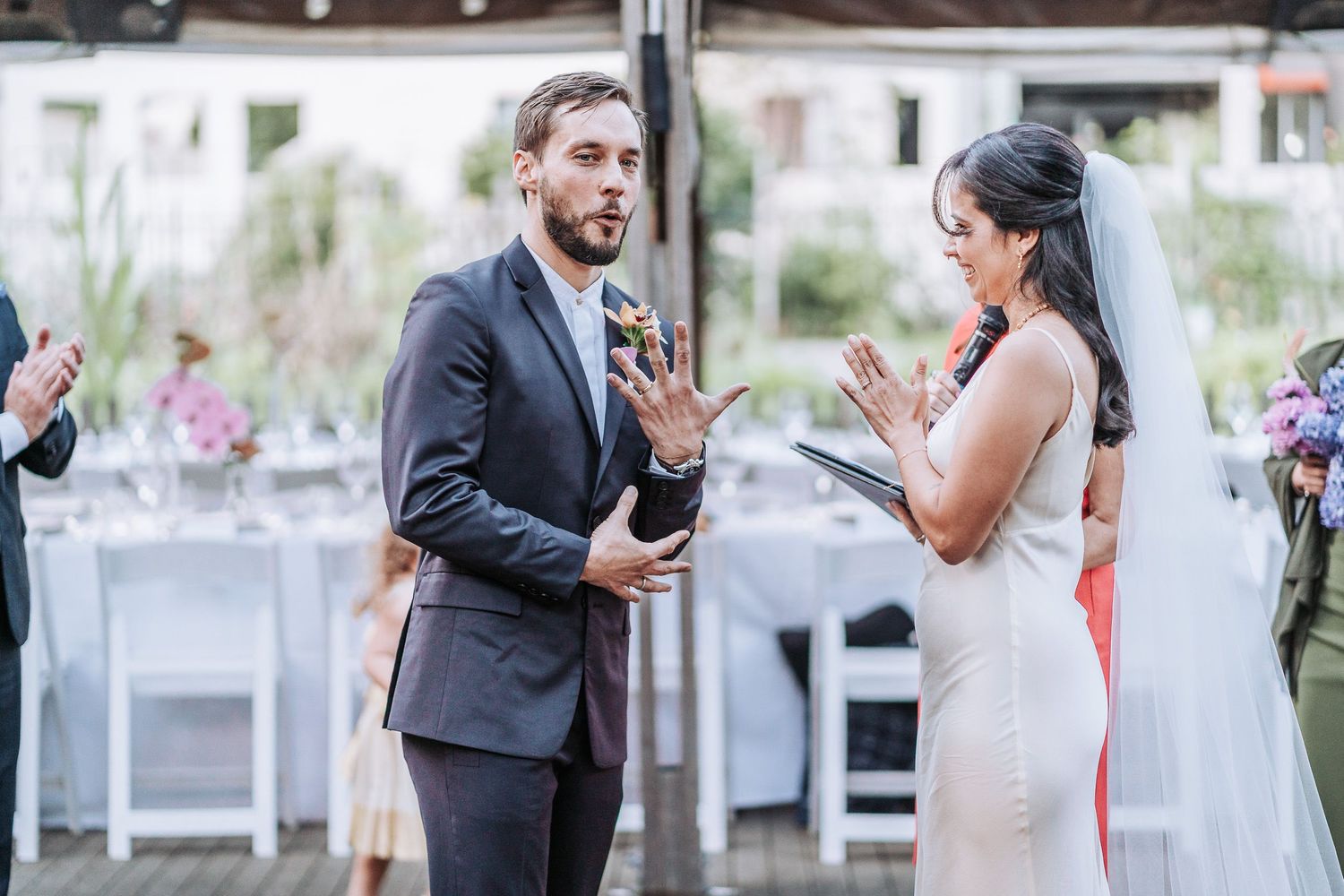 Two people share an emotional moment during an outdoor wedding ceremony with decorated tables and florals in the background.