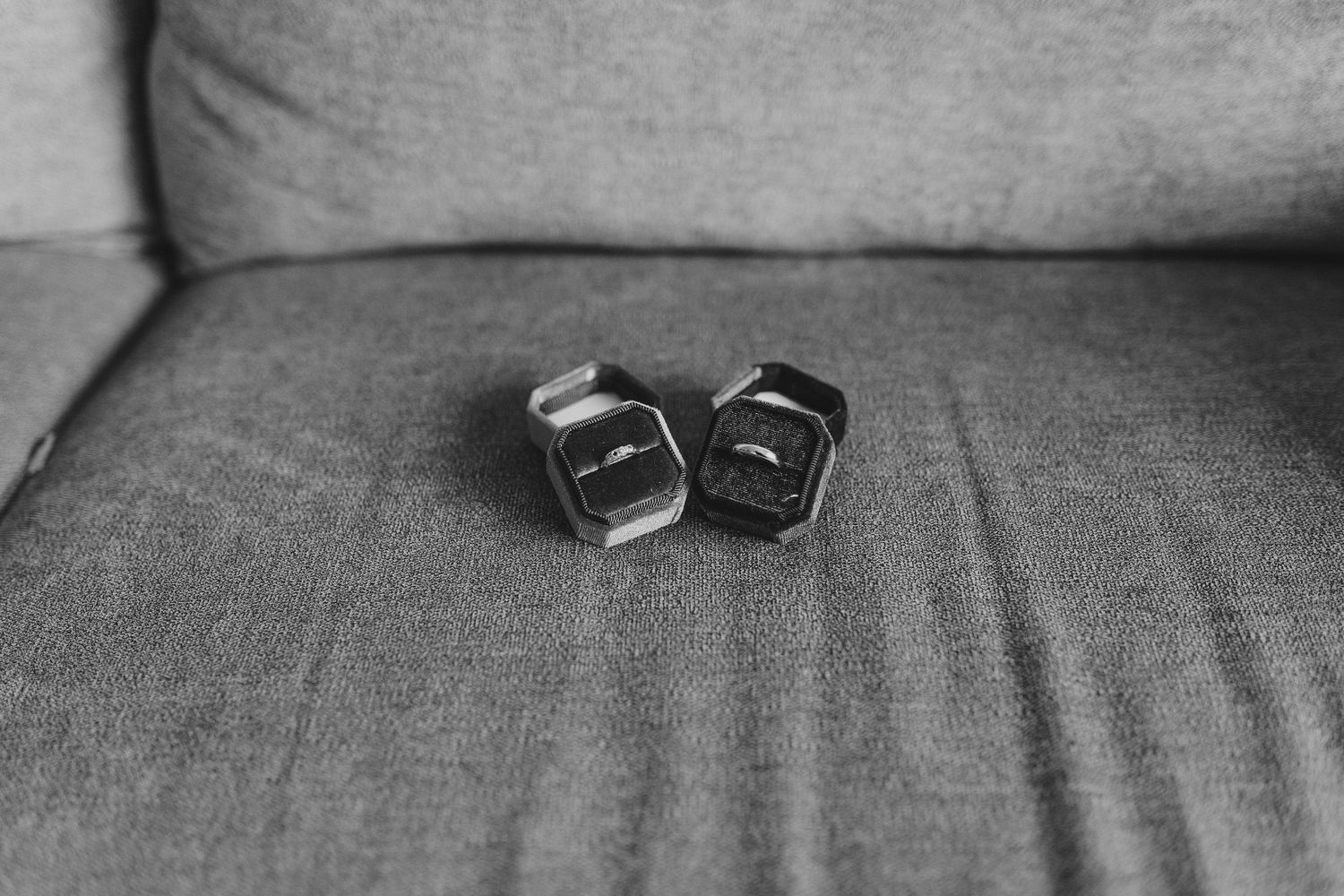 A pair of black gaming dice sitting on a gray fabric couch in monochromatic black and white photography.