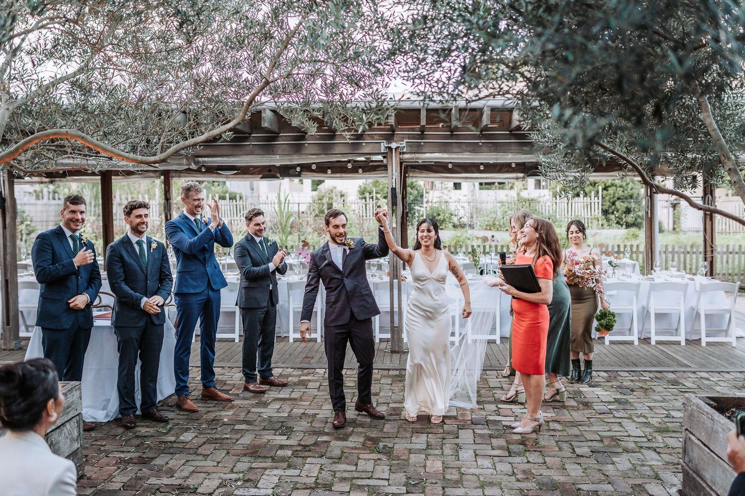 Wedding party celebrates on vintage brick patio under blooming cherry blossom trees during spring ceremony.
