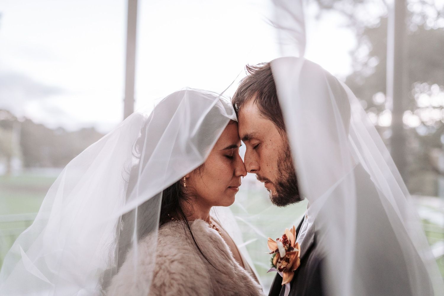 A romantic moment shared under a wedding veil as a couple touches foreheads during their wedding ceremony.