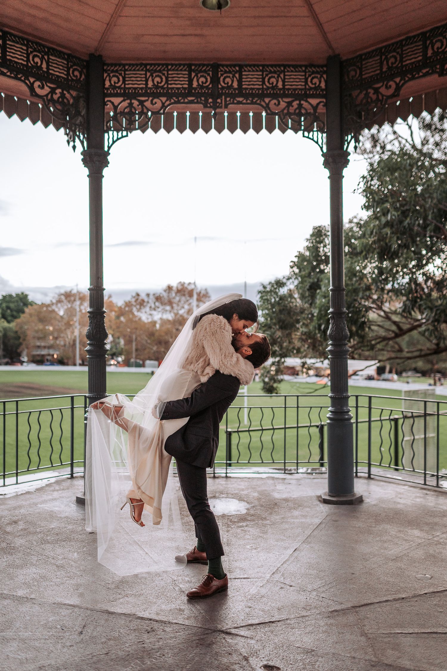 Victorian gazebo in park setting with couple embracing in romantic dip pose during autumn day.