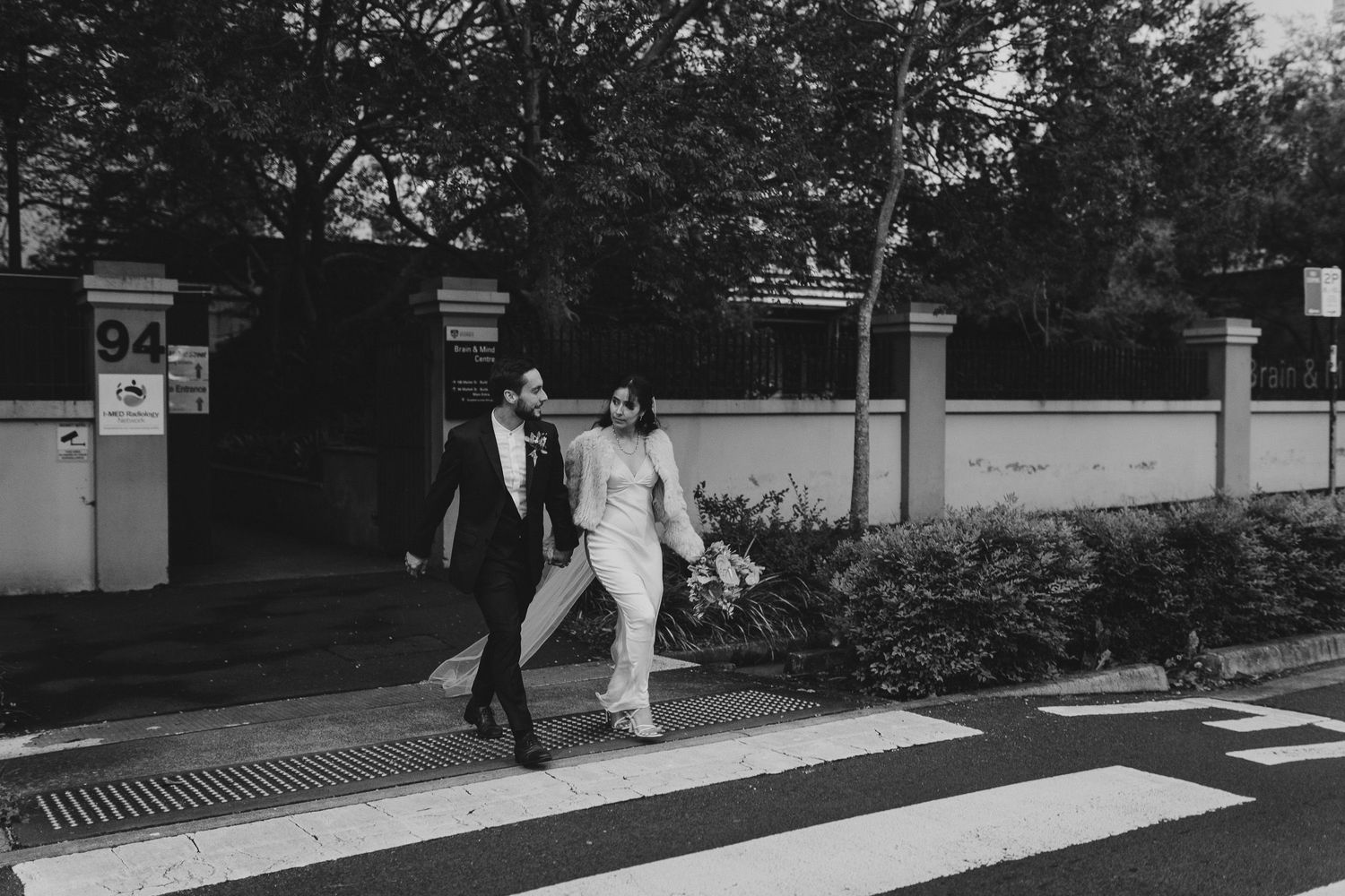 A couple in formal attire crosses a pedestrian walkway together in black and white photography.